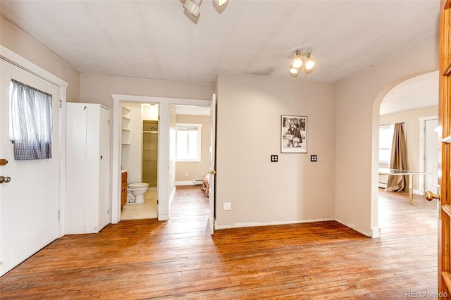 entryway featuring arched walkways, light wood-style floors, and a baseboard radiator