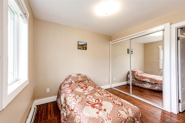 bedroom featuring wood finished floors, a closet, baseboards, and a baseboard radiator