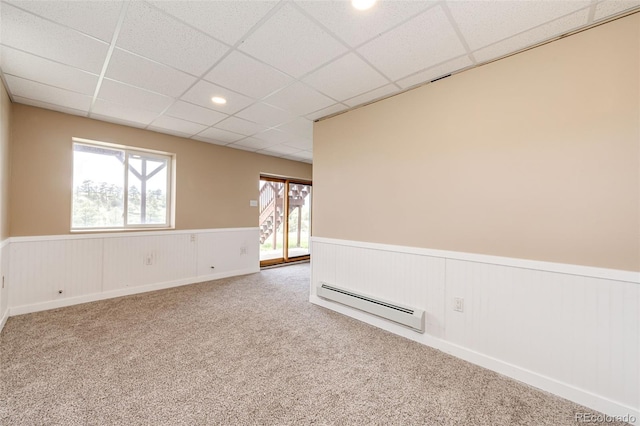 carpeted spare room featuring baseboard heating, a wainscoted wall, plenty of natural light, a drop ceiling, and recessed lighting