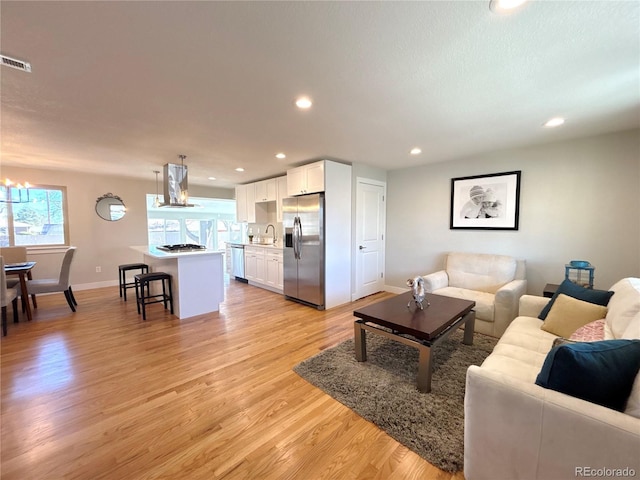 living room with light wood-style flooring, visible vents, baseboards, and recessed lighting