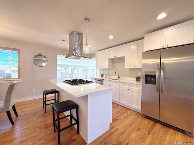 kitchen featuring island range hood, a sink, light countertops, appliances with stainless steel finishes, and light wood finished floors