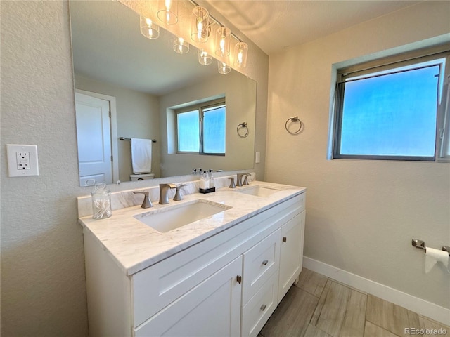 full bath featuring wood finish floors, a sink, baseboards, and double vanity