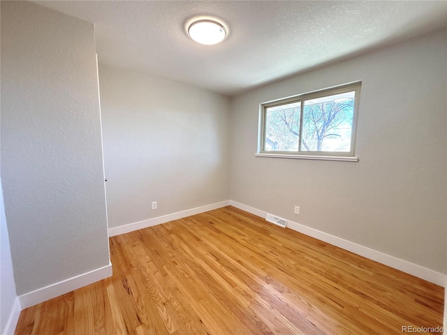 unfurnished room with light wood-type flooring, visible vents, a textured ceiling, and baseboards