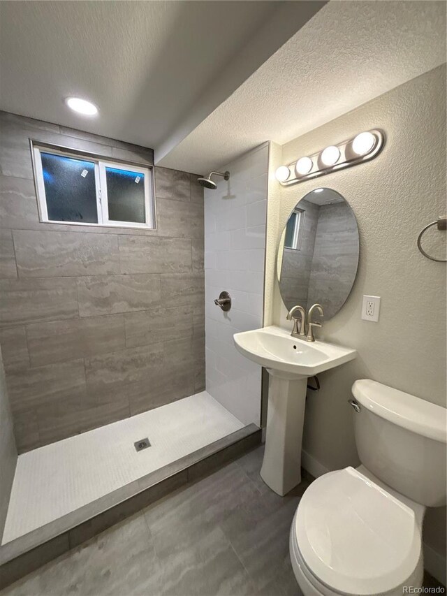 bathroom featuring a textured ceiling, a textured wall, tiled shower, and toilet