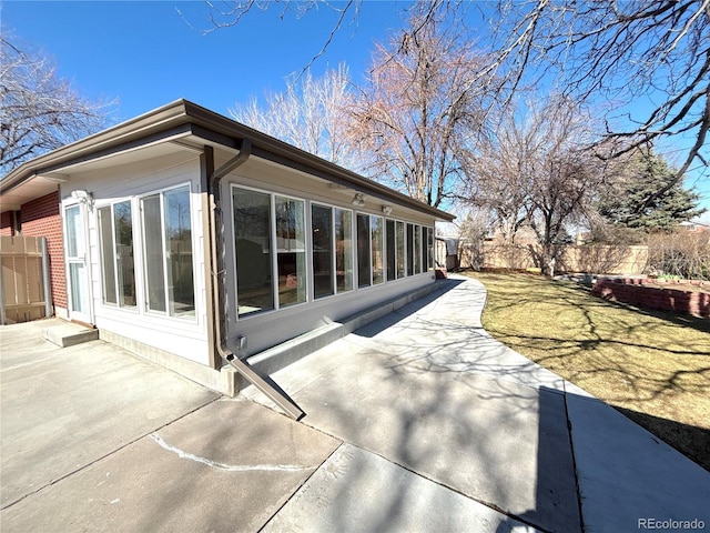 view of side of home featuring a patio, brick siding, fence, and a sunroom