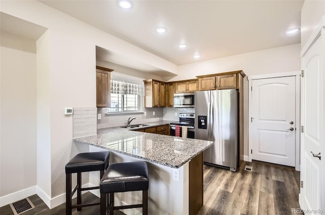 1746 Westward Cir Unit 1, Eaton, CO 80615 - kitchen featuring appliances with stainless steel finishes, a peninsula, brown cabinets, light stone countertops, and dark wood-style flooring