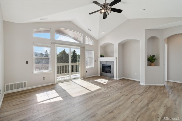 unfurnished living room with a ceiling fan, lofted ceiling, light wood finished floors, visible vents, and a tile fireplace