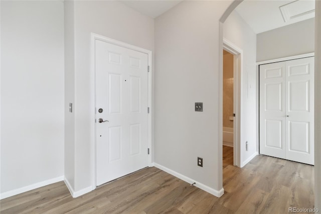 foyer with arched walkways, baseboards, and light wood finished floors