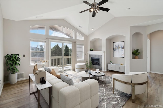 living room with a ceiling fan, wood finished floors, a tile fireplace, and vaulted ceiling