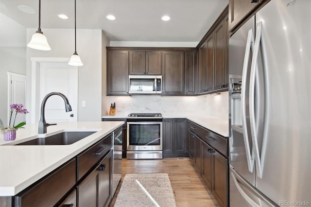 kitchen featuring light wood finished floors, appliances with stainless steel finishes, dark brown cabinetry, and a sink
