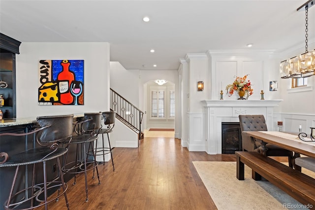 bar featuring arched walkways, a decorative wall, a bar, wood finished floors, and stairs