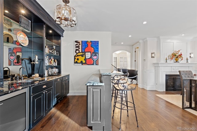 bar featuring arched walkways, dark wood finished floors, a fireplace with flush hearth, wet bar, and a sink