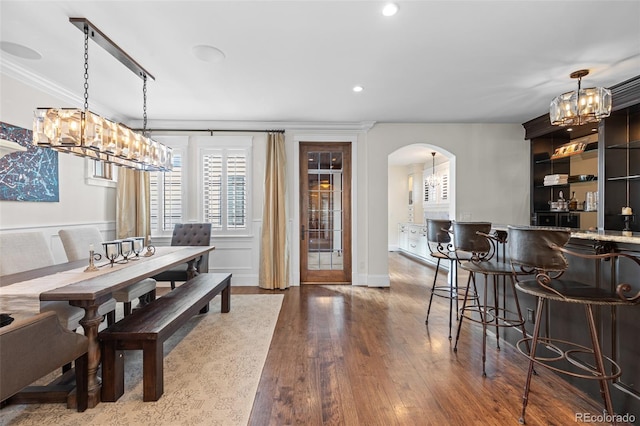 dining room with recessed lighting, arched walkways, wood finished floors, and ornamental molding