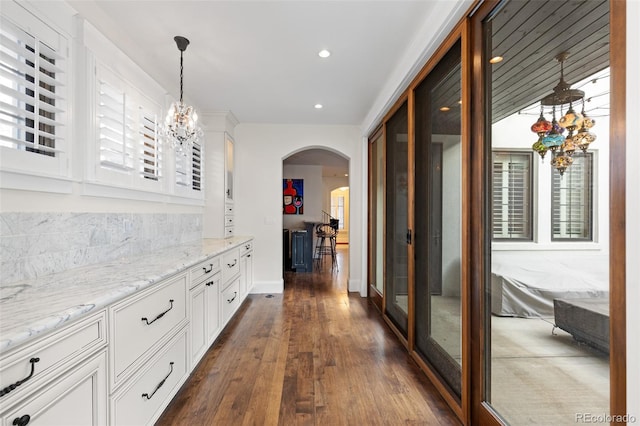 hall featuring arched walkways, dark wood-style flooring, a notable chandelier, recessed lighting, and baseboards