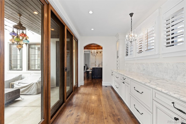 hall featuring arched walkways, recessed lighting, baseboards, dark wood-style floors, and an inviting chandelier