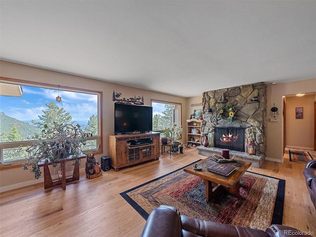 living room featuring a stone fireplace, baseboards, and light wood finished floors