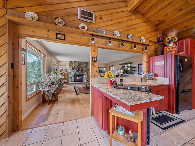 kitchen with open floor plan, light tile patterned flooring, a peninsula, black appliances, and a fireplace