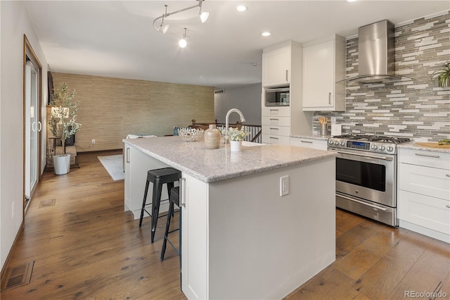 5292 W Fair Dr, Littleton, CO 80123 - kitchen featuring stainless steel appliances, wall chimney range hood, a breakfast bar, white cabinets, and dark wood-type flooring
