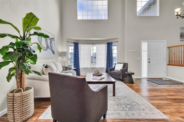 living room featuring an inviting chandelier, a towering ceiling, and wood-type flooring