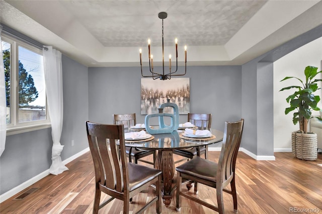 dining area with hardwood / wood-style flooring, a notable chandelier, a tray ceiling, and a wealth of natural light