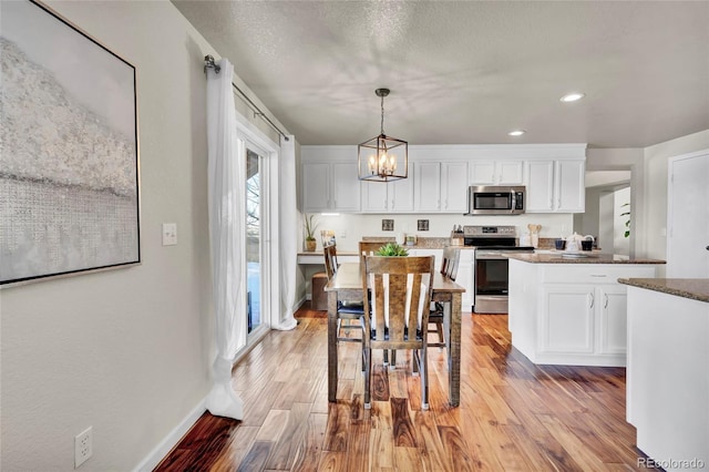 kitchen featuring pendant lighting, stainless steel appliances, a notable chandelier, white cabinets, and light wood-type flooring