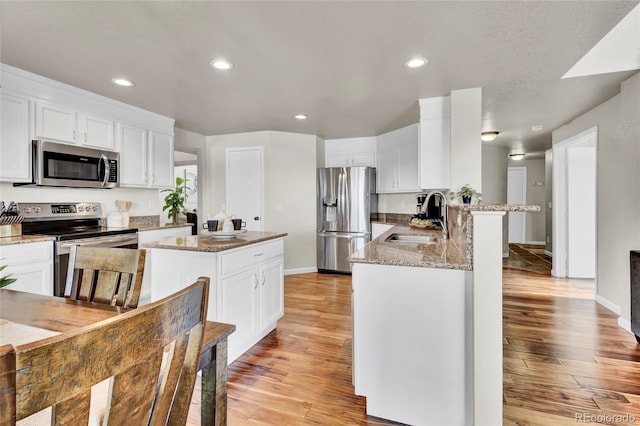 kitchen featuring sink, appliances with stainless steel finishes, light stone counters, white cabinets, and kitchen peninsula