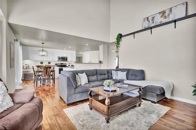 living room with a towering ceiling, light hardwood / wood-style floors, and a chandelier