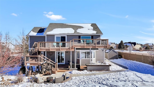 snow covered house featuring a wooden deck and a storage unit