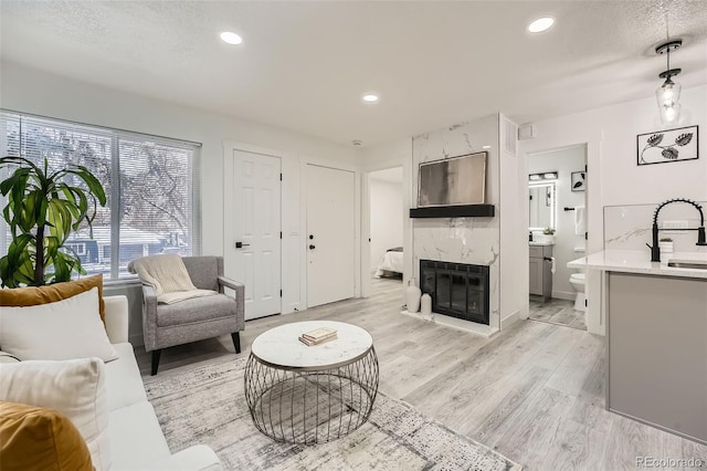 living room featuring a premium fireplace, sink, light hardwood / wood-style floors, and a textured ceiling