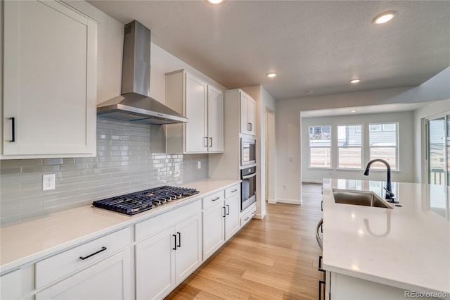 8595 Silverton Ln, Littleton, CO 80125 - kitchen featuring sink, stainless steel gas cooktop, wall chimney range hood, white cabinetry, and light wood-type flooring