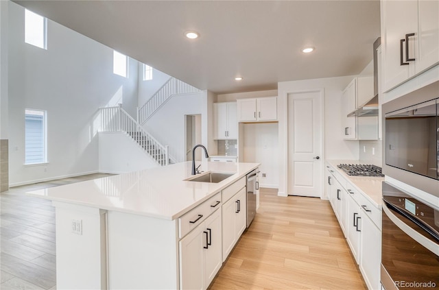 8595 Silverton Ln, Littleton, CO 80125 - kitchen with a kitchen island with sink, stainless steel appliances, white cabinets, sink, and light hardwood / wood-style floors