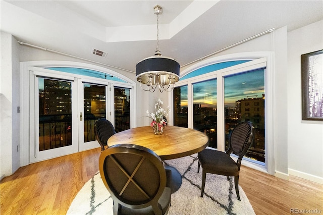 dining room with a raised ceiling, light wood-style floors, a chandelier, and baseboards