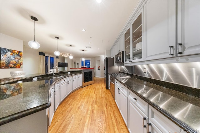 kitchen with stainless steel appliances, light wood-style flooring, a sink, and glass insert cabinets