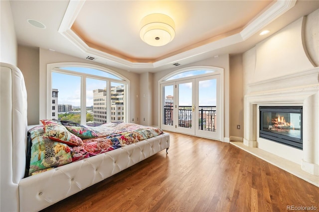 bedroom featuring a raised ceiling, access to outside, a large fireplace, wood finished floors, and french doors