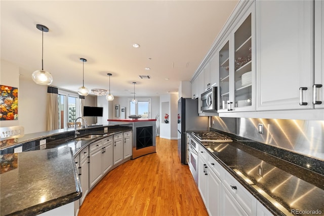 kitchen featuring appliances with stainless steel finishes, a sink, light wood-style flooring, glass insert cabinets, and hanging light fixtures