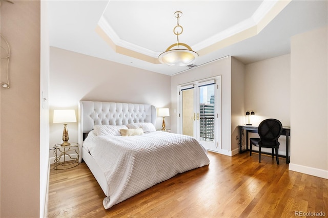 bedroom featuring a tray ceiling, access to exterior, crown molding, wood finished floors, and baseboards