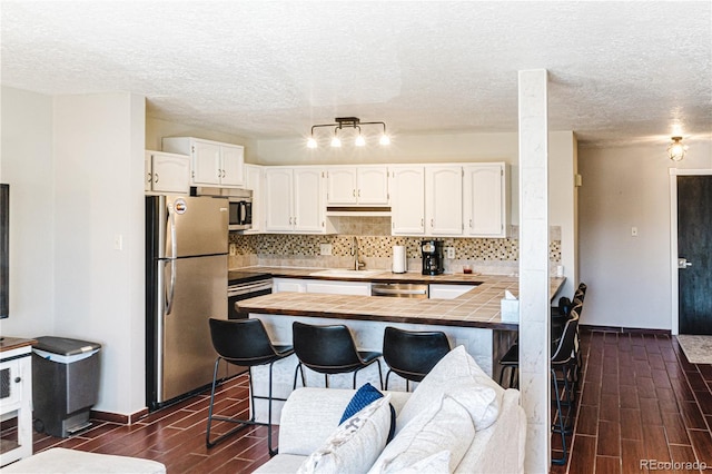 kitchen with sink, appliances with stainless steel finishes, dark hardwood / wood-style flooring, white cabinetry, and a breakfast bar area