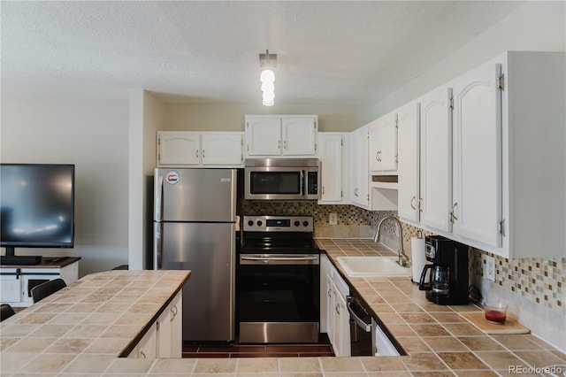 kitchen with decorative backsplash, appliances with stainless steel finishes, sink, white cabinets, and tile counters