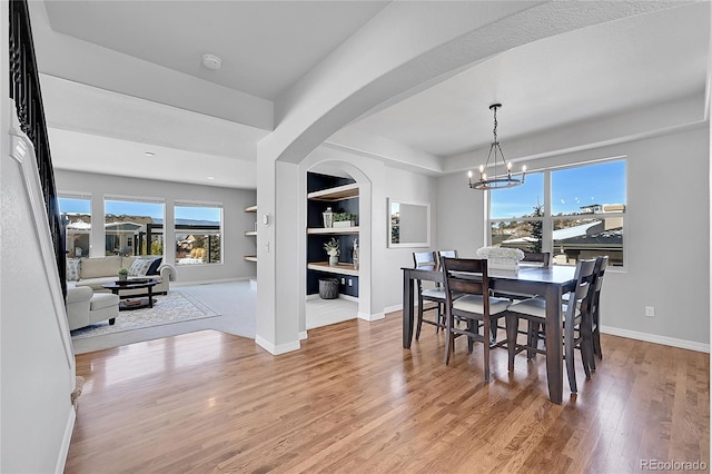 dining space with built in features, a chandelier, and light wood-type flooring