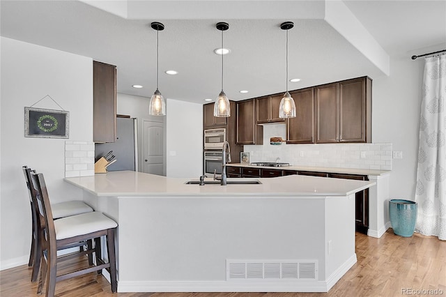 kitchen featuring kitchen peninsula, sink, hanging light fixtures, and light hardwood / wood-style flooring