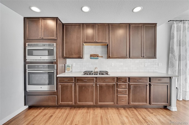 kitchen featuring dark brown cabinetry, stainless steel appliances, light hardwood / wood-style floors, and decorative backsplash