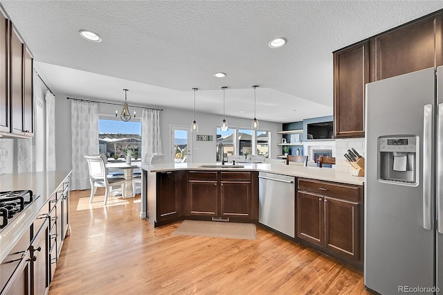 kitchen with sink, hanging light fixtures, appliances with stainless steel finishes, kitchen peninsula, and light hardwood / wood-style floors