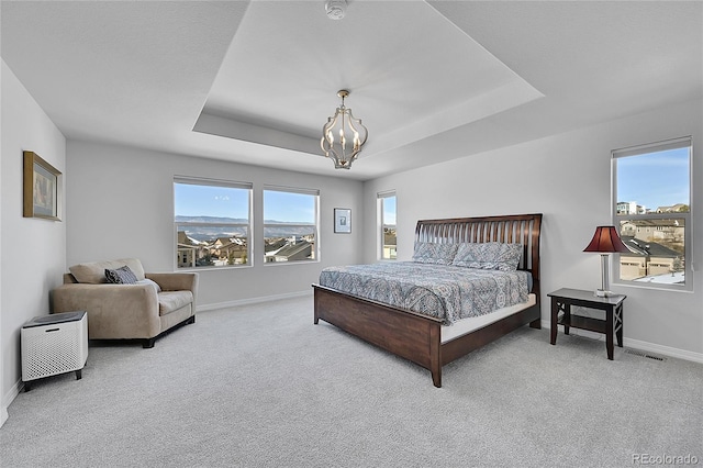 bedroom with light colored carpet, a raised ceiling, and multiple windows