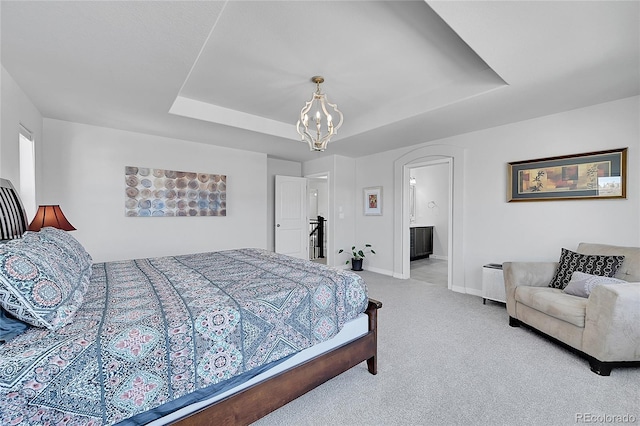 carpeted bedroom with connected bathroom, a notable chandelier, and a tray ceiling