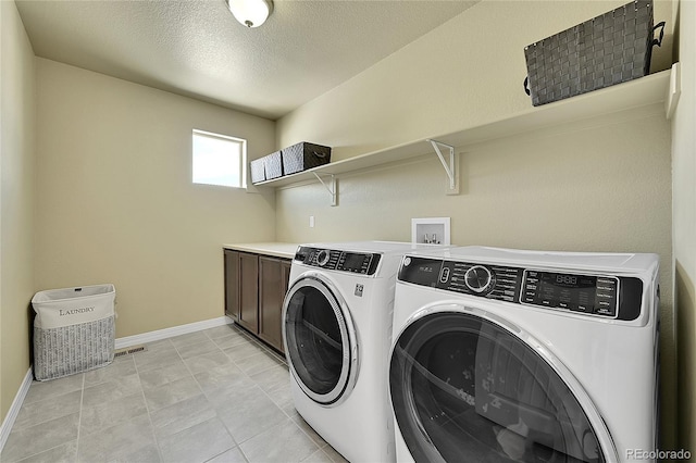 washroom with cabinets, washing machine and dryer, light tile patterned floors, and a textured ceiling