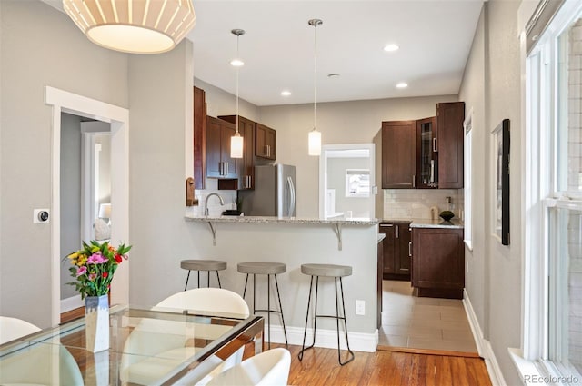 1532 Meade St, Denver, CO 80204 - kitchen featuring freestanding refrigerator, a kitchen bar, light wood finished floors, decorative backsplash, and glass insert cabinets