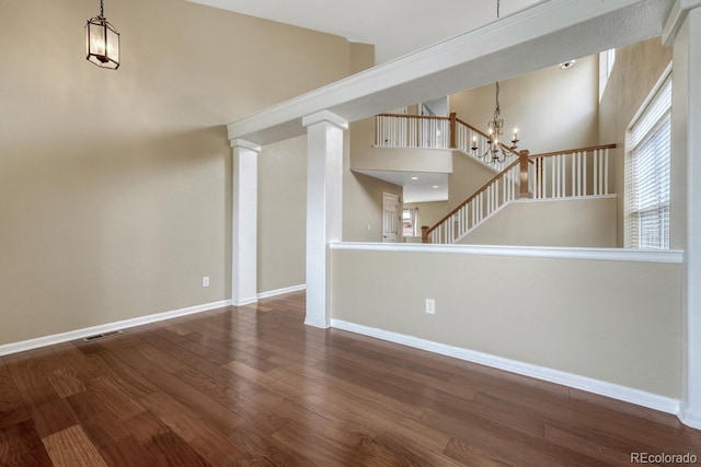 unfurnished living room featuring a chandelier, wood finished floors, baseboards, and stairway