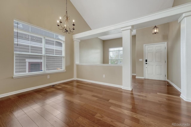 unfurnished dining area featuring a chandelier, wood finished floors, baseboards, high vaulted ceiling, and decorative columns