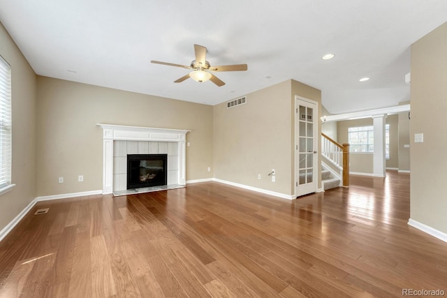unfurnished living room with a ceiling fan, stairway, a fireplace, wood finished floors, and baseboards