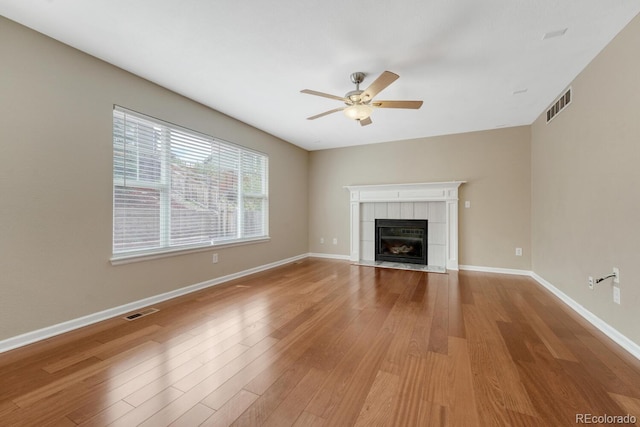 unfurnished living room featuring ceiling fan, light wood finished floors, a tiled fireplace, and baseboards